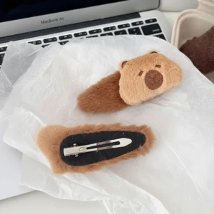 Close-up of a fuzzy, brown plush capybara hair clip with embroidered face details and a soft stuffed texture.