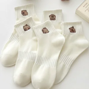 Fünf Paar weiße Capybara Socken mit unterschiedlichen bestickten Designs auf einem Tisch