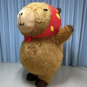 Aufblasbares Capybara Kostüm mit rotem Tupfelbandana und roter Fliege, Ganzkörperansicht vor blauem Hintergrund