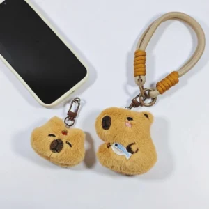 Beide Varianten des capybara plüsch anhänger handy armband zusammen neben einem smartphone dargestellt