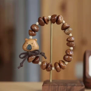Rustikales Capybara Armband mit geschnitztem Pfirsichholz-Capybara-Kopf und Schleife, aufgereiht mit braunen kaffeebohnenförmigen Kuka-Nuss Perlen, präsentiert auf einem Holzständer