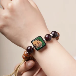 Detailansicht Capybara Armband aus Thuja-Holz mit bemaltem Capybara Motiv auf grünem Hintergrund und Quaste