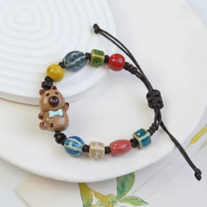 Nahaufnahme von zwei verstellbaren gewebten Capybara Armbändern mit glasierten Keramik-Capybara-Charms in braunen und beigen Tönen, Design 1