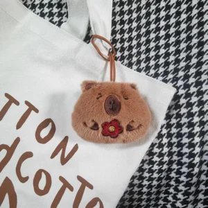 Capybara Plüsch Namensanhänger mit Glücksblume hängt an einer weißen Canvas-Tasche