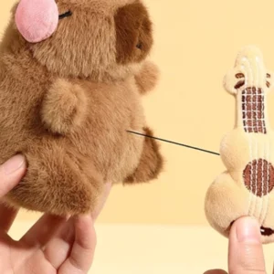 hand zieht die plüsch-gitarre vom capybara körper weg, zeigt das ausziehbare zugseil des capybara plüsch-schlüsselanhängers