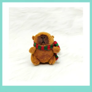 Sitzender Capybara Plüsch-Anhänger mit festlichem Winter Schal und weißen Bommel, auf weißem Hintergrund