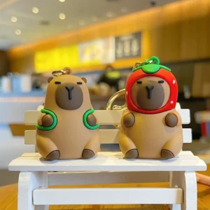 Capybara Schlüsselanhänger zwei Modelle im Vergleich, weiches PVC mit Erdbeerhaube und Schildkrötenrucksack, mit goldenem Verschluss