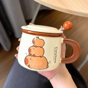 Cremefarbene Keramik Capybara Tasse mit drei gestapelten Capybaras, Text 'Emotional Stability', passendem Deckel und Löffel mit orangefarbener Perle