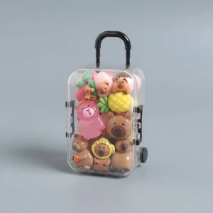 Durchsichtiger Mini Rollkoffer gefüllt mit rosa und braunen Mini Capybara Figuren die im Dunkeln grün leuchten