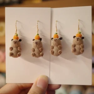 Handgehäkelte Capybara Ohrringe, zwei Designs: eine mit kleiner Orange auf dem Kopf, eine mit roter Weihnachtsmannmütze