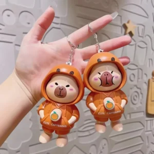 Hand drückt die Brusttaste des niedlichen interaktiven Capybara Schlüsselanhängers aus orange, zeigt den Gesichtswechsel-Mechanismus