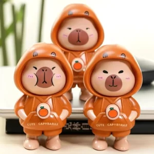 Hand drückt die Brusttaste des niedlichen interaktiven Capybara Schlüsselanhängers aus PVC mit orangem Hoodie, zeigt den Gesichtswechsel-Mechanismus