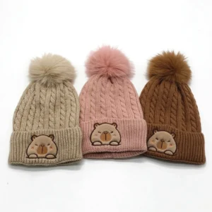 Kollektion der Kinder Capybara Beanie in drei Farben (beige, rosa, braun) mit Zopfmuster und flauschiger Bommel