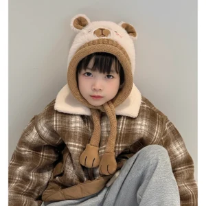 Kind trägt flauschige cremefarbene Capybara Beanie mit braunem Strickrand und langen Ohrenklappen, die in weiche Plüschpfoten enden