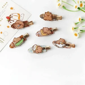 flache aufnahme von sechs verschiedenen capybara haarspangen aus acryl mit karo muster mit motiven wie capybara mit messer, gans umarmen und krokodil reiten