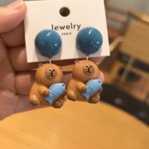 Nahaufnahme der süßen Capybara Ohrringe mit hellblauem Fisch, niedliches Capybara Accessoire für Fans