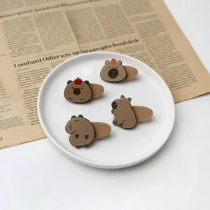 Draufsicht von vier flachen Acryl Capybara Haarspangen, zwei mit Vorderseiten mit Frucht auf dem Kopf, zwei mit Seitenprofil-Posen