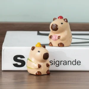 Zwei handbemalte Capybara Keramik Mini Figuren in Meditationshaltung, eine mit rosa Krone und eine mit Gebetskugeln, auf Holzuntergrund, Capybara Figur