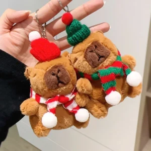 Zwei Weihnachts Capybara Plüsch-Schlüsselanhänger hängen als Weihnachtsbaumschmuck an einem Tannenzweig